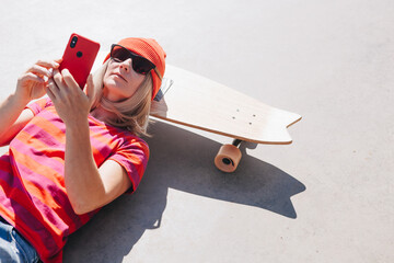 Beautiful young hipster woman using smart phone On Skateboard at summer day. Active lifestyle, modern life, subculture concept