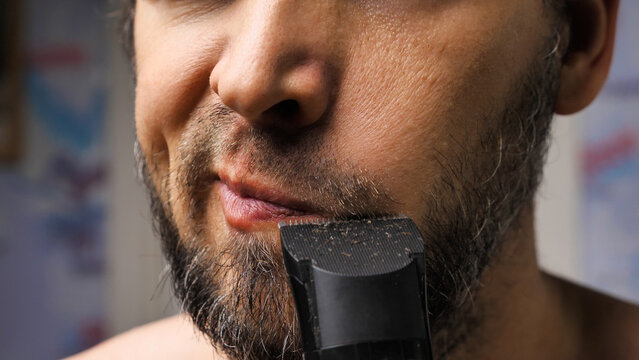 A Man Trims His Beard With A Trimmer. Close Up. An Electric Razor Trimming A Beard. Black Beard With Grey Hairs. Beard Care At Home.