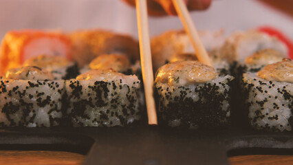 A traditional Japanese seafood dish. Close-up. Chopsticks are taken from a black stone plate of sushi rolls. Assortment of sushi, rolls, Asian food with fresh ingredients on dark background.