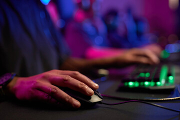 Close up of unrecognizable person playing videogames in neon light with focus on hand holding computer mouse, copy space