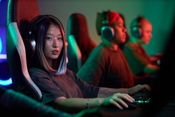 Portrait of tattooed young Asian woman playing video games professionally and looking at camera in...