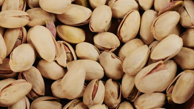 Salted pistachios falling down on red plate close-up macro. Nuts snacks for parties, fried crispy pistachios with cracked shells for beer 