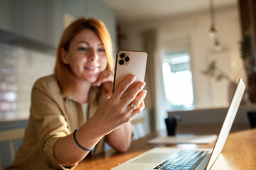 Cheerful woman using her smartphone in a bright kitchen