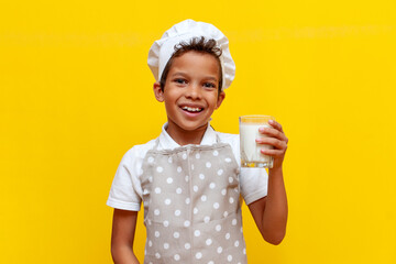 african american boy in chef's uniform and hat holding glass of milk on yellow isolated background
