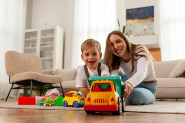 young mother with her little son playing at home with toys on the floor, 2 year old boy holding toy...