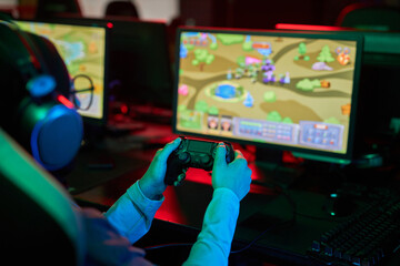 Close up of female gamer playing video game in eSports club with focus on hands holding controller in neon light, copy space