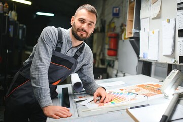 Print house worker controlling printing process quality and checking colors with magnifying glass