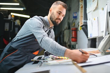 Print house worker controlling printing process quality and checking colors with magnifying glass