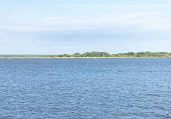 Ocean with a narrow coastline and blue sky. Summer day with soft whispy clouds.
