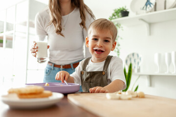 funny little boy 2 years old eats breakfast himself in the kitchen with a dairy product, the child...