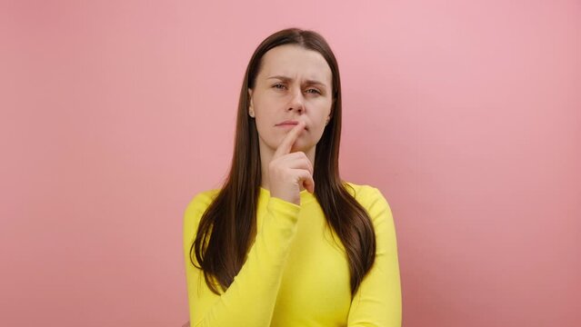 Overjoyed happy cute young woman pointing finger up looking at camera with toothy smile, having idea, startup, wearing yellow sweater, isolated on pink color background wall in studio. Plan concept