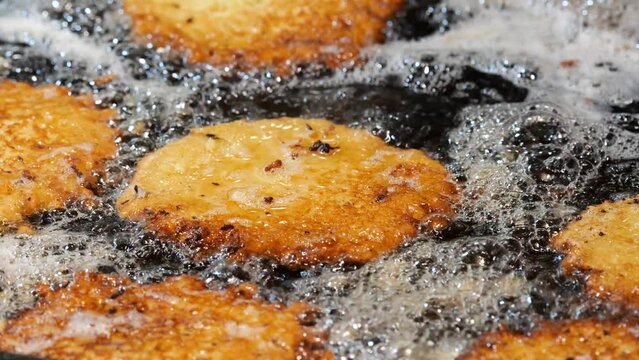 Traditional Polish potato pancakes food deep fried in oil, frying food slow motion bubbling oil crispy golden hash browns cooking on a pan, fat, oil, fatty foods concept, nobody, detail closeup shot