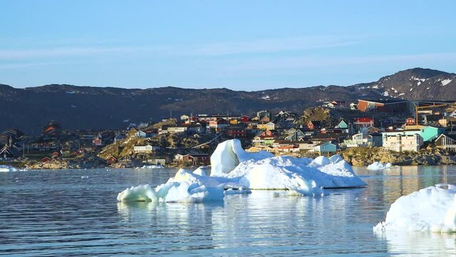Ocean, icebergs and Greenland settlement. Greenland arctic village Ilulissat. Colorful inuit houses. Greenland polar landscape. Travel to the Arctic Circle. Climate change, global warming.