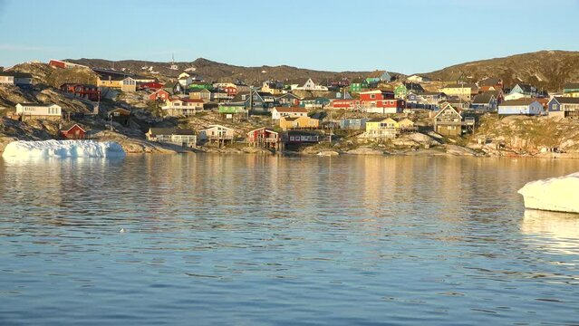 Ocean, icebergs and Greenland settlement. Greenland arctic village Ilulissat. Colorful inuit houses. Greenland polar landscape. Travel to the Arctic Circle. Climate change, global warming.