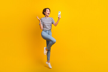 Fototapeta na wymiar Full body portrait of impressed carefree lady jump use smart phone empty space ad isolated on yellow color background