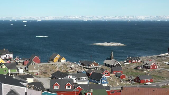 Ocean, icebergs and Greenland settlement. Greenland arctic village Ilulissat. Colorful inuit houses. Greenland polar landscape. Travel to the Arctic Circle. Climate change, global warming.