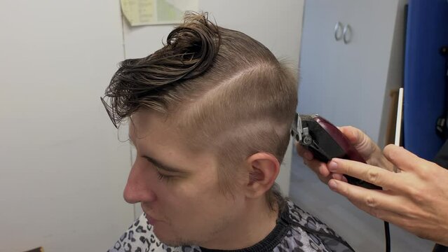 Hands of barber cutting hair of caucasian man with a trimmer and comb. Self care lifestyle. Trendy modern hairstyle in beauty salon. Hairdo. Shaves his hair with an electric razor. slow motion