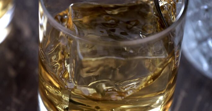 Super Slow Motion Detail Shot of Pouring old malt burbon Whiskey on Ice Cubes into pure Glass at 1000fps.