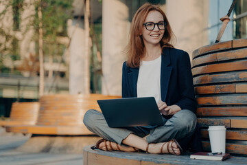 Relaxed businesswoman working on her laptop while sitting outside, with coffee and notebook