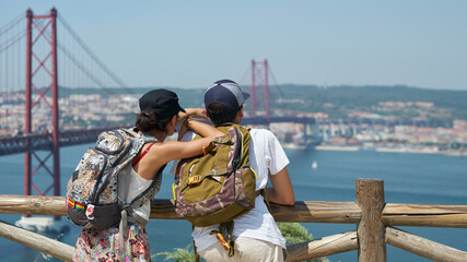 Tourists (young married couple) look at the suspension bridge over the Tagus River in Lisbon from the observation deck. - obrazy, fototapety, plakaty