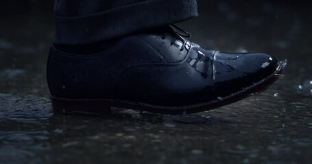 Super slow motion macro of businessman elegant shoe is going through puddle of rain water with splashing drops on asphalt street.