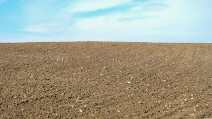 Ploughed farm field under a clear cloudy blue sky in an agricultural landscape. Open space area.

