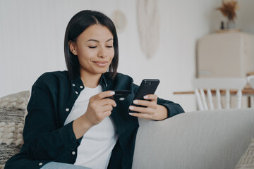 Smiling young woman using smartphone for online banking at home