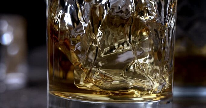 Super Slow Motion Detail Shot of Pouring old malt burbon Whiskey on Ice Cubes into pure Glass at 1000fps.