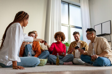 multiracial group of young people sitting at home with beer and popcorn and playing cards with friends