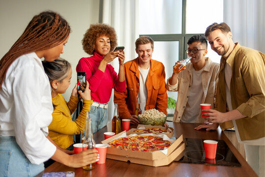 multiracial group of young people at house party ordered pizza and beer and photographed the food on the phone