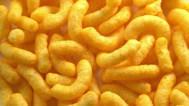 Cheesy corn chips rotates on plate top view. Crispy cheese snack. Crispy fluffy corn sticks for breakfast