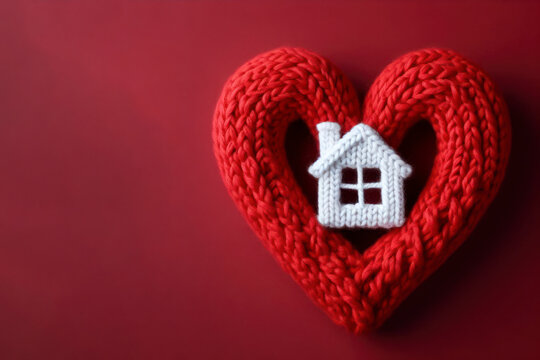 Knitted red heart shaped with white house on red background. ai generative