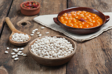 High angle photo of a bowl of navy beans on a vintage wooden table with traditional home cooked navy beans dish on a linen napkin in the background