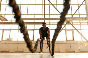 african american athletic man in sportswear training in the gym and waving the ropes, athlete doing...