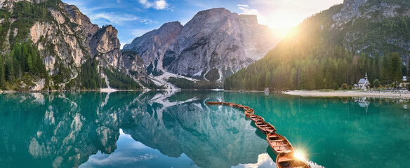 Panoramic photo of Lago di Braies, Pragser Wildsee in the Dolomites. View of the whole green-blue lake through wooden boats on the mountain peak and the setting sun.