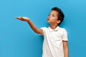african american boy in white polo blows kiss on blue isolated background