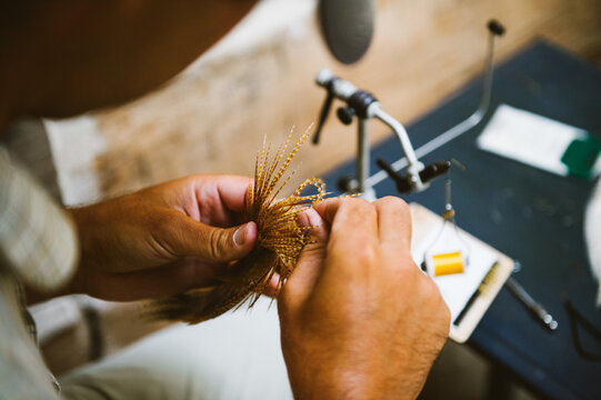 A man ties a tiny fishing fly on a table in a cabin, macro