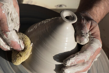 The hands of a master potter working his product on a potter's wheel.