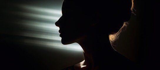 a silhouette of a woman's head in a dark room with light coming through the blinds on the wall.