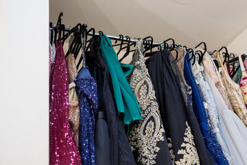 Different evening gown dresses on hangers in boutique. Pink, blue and gray sequined luxury dresses for woman hang on hangers.Row of different beautiful cloth.dress rent shop