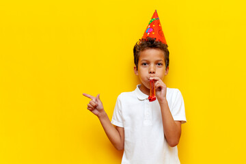 African American boy in festive hat celebrates his birthday and blows trumpet on blue isolated...