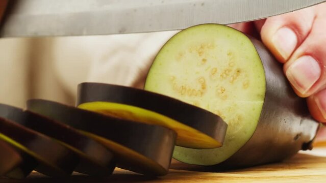 Cutting purple eggplant on wooden desk with knife close-up macro. Slicing aubergine . Woman hand cut vegetables. Food healthy concept