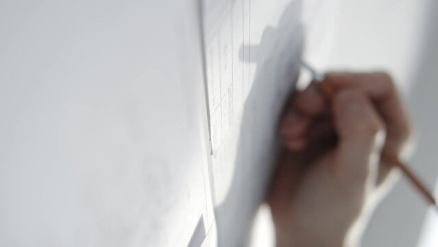 Architect writes on a drawing hanging on the wall. Close-up, hand with a pencil in the frame.