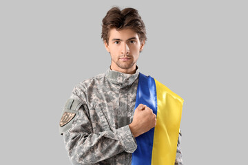 Young male soldier with Ukrainian flag on grey background