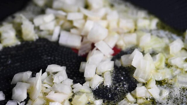Chopped onions mixing in a frying pan with vegetable oil.