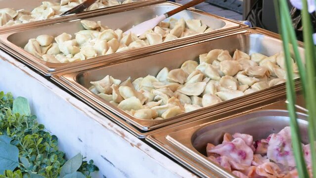 Lots of different flavored traditional classic Polish pierogi with different stuffings on sale, metal container food festival market stall, restaurant service. Local kitchen food culture concept