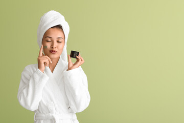 Beautiful Asian woman applying facial mask on green background
