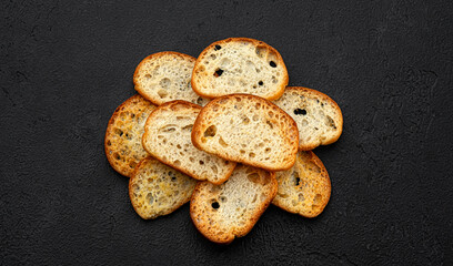 Bruschetta crackers, bread croutons on black background, top view