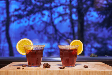 Two glasses of spiced or mulled wine in front of window during sold and freezy winter sunset. Mulled wine is typical and traditional drink for christmas time in Germany, Austria and Czech republic.