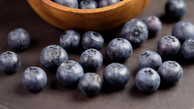 A pile of fresh blue bilberry on a brown board with wooden bowl. Ripe blueberries. Healthy bio food. Rotation